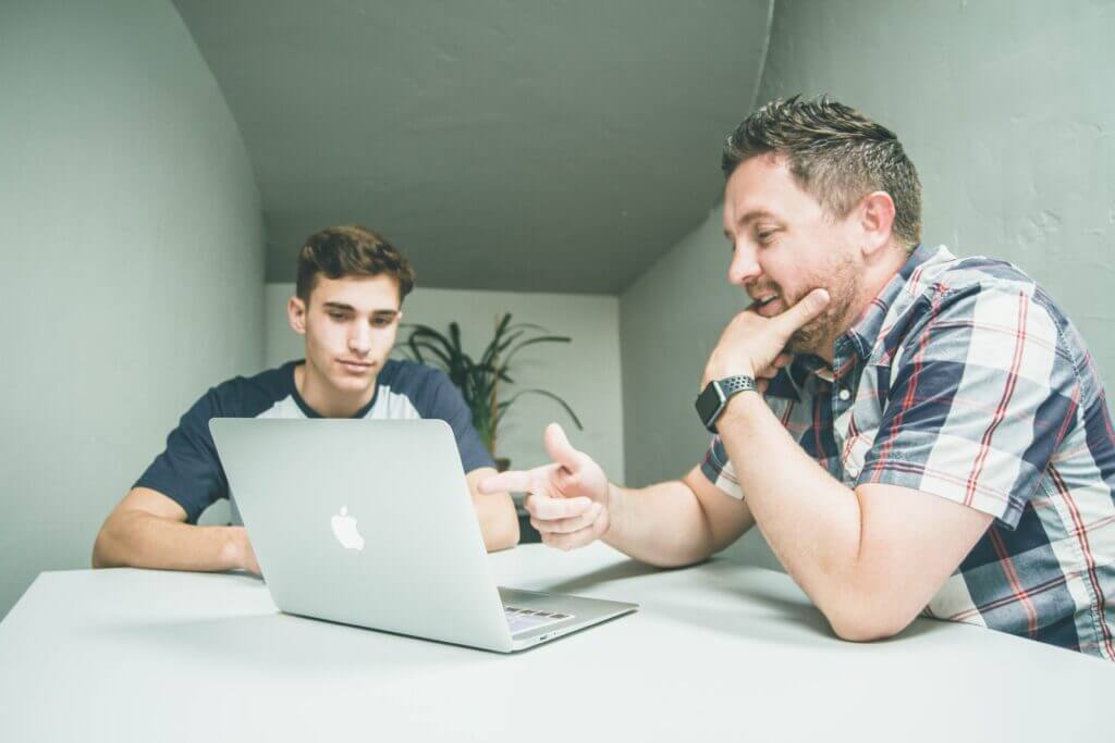 Man wearing white and black plaid button-up sports shirt pointing the silver macbook - inriver pim consulting and solutions