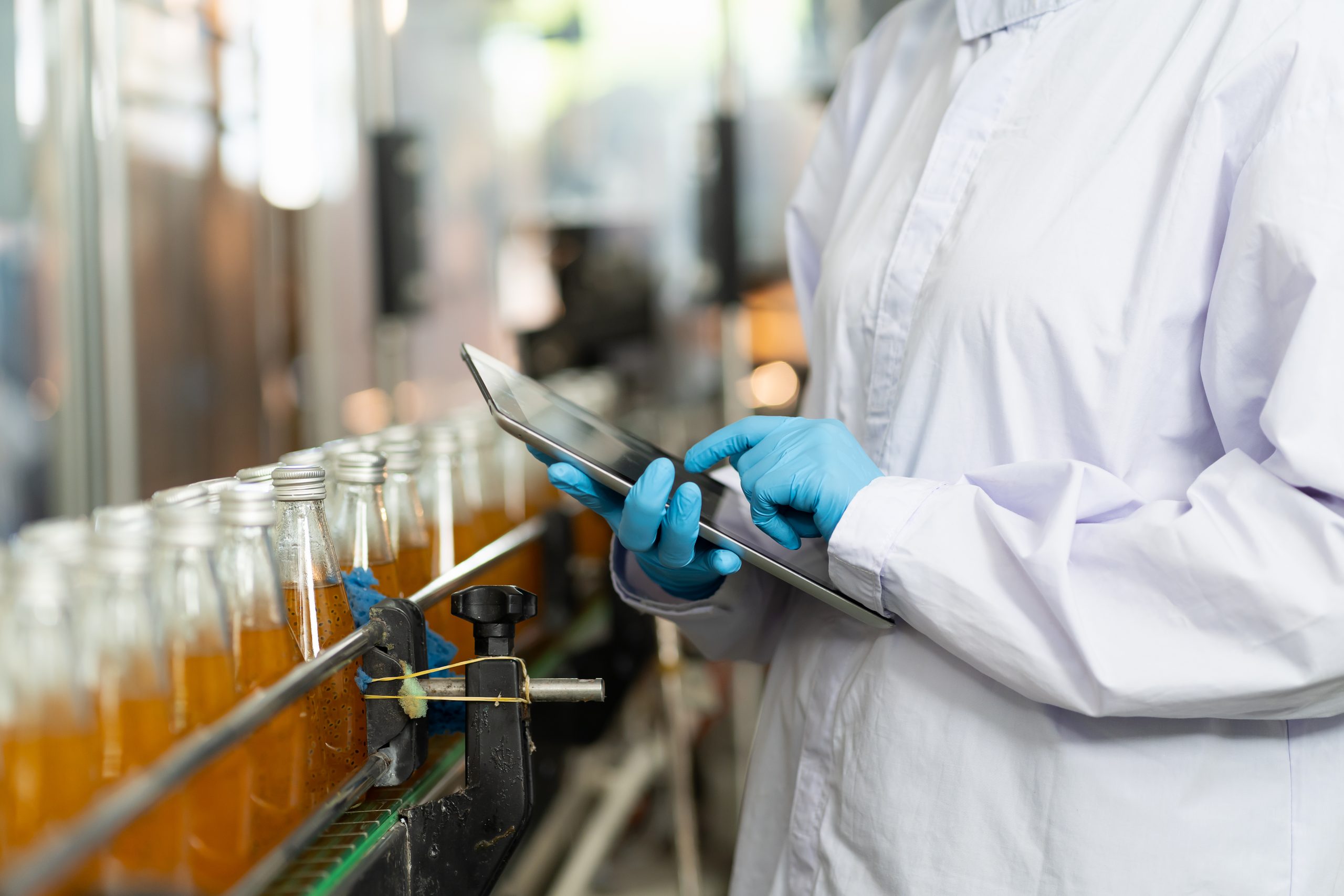 Manufacturing technician using tablet to monitor production line with custom software solutions for quality control and efficiency.- technology implemented with custom manufacturing software development services